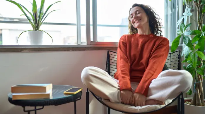 Smiling woman in orange sweater relaxing indoors — feeling emotionally lighter, confident, and aligned after healing inner blocks
