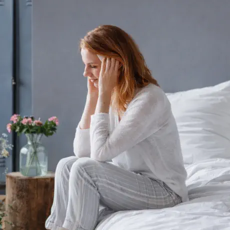 Woman sitting on a bed in quiet distress, representing emotional pain and the need for healing